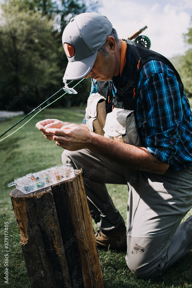 Wall mural Close up shot of senior fisherman's hands tying a fly for fishing. Fly fishing concept.