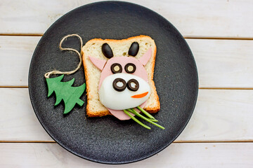 Christmas funny breakfast toast bull for kids. Creative children's sandwich in the shape of a bull made from toast, sausages, eggs on black plate. Bull cow Symbol of the year 2021, copy space