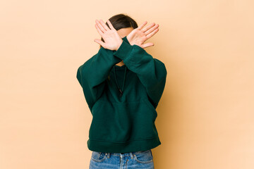 Young woman isolated on beige background keeping two arms crossed, denial concept.