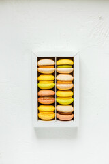 Colorful french macarons in a white box on white background, top view