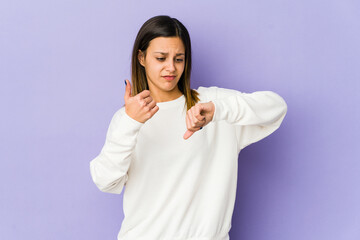 Young woman isolated on purple background showing thumbs up and thumbs down, difficult choose...