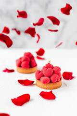 Sweet dessert tartelettes with red mousse hearts on top, decorated with red rose petals