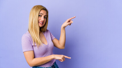 Young blonde woman isolated on purple background shocked pointing with index fingers to a copy space.