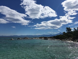 Sunny rock beach in Greece with clody sky with trees on background