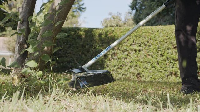 Slow motion of a string trimmer cutting weeds and grass in a garden