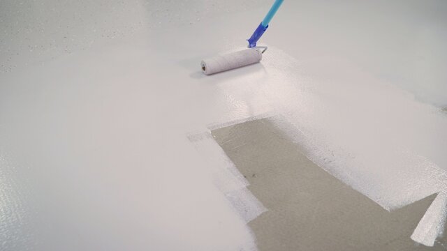 A worker paints the concrete floor with a roller white. Concrete Floor repair work. Paint roller in construction site