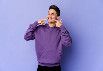Young caucasian man isolated on purple background smiles, pointing fingers at mouth.