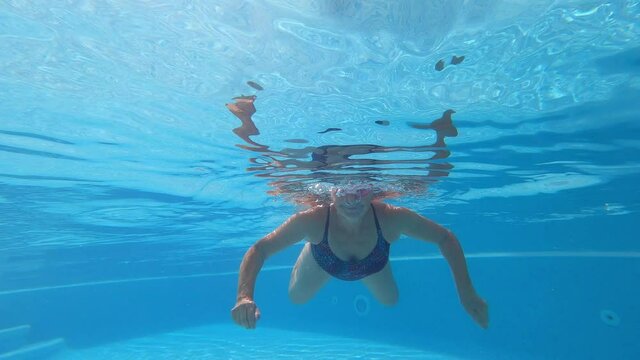 one mature woman alone doing exercise alone underwater having fun and looking at the camera waving at it - vacations and summer lifestyle swimming in a pool looking at the camera smiling and enjoying