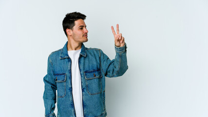 Young caucasian man isolated on white background joyful and carefree showing a peace symbol with fingers.
