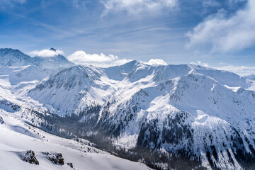 View from Kasprowy Wierch at pine forest with winter coating in the valley. Snow capped mountain peaks of Tatra Mountains, Bukowina Tatrzanska, Poland
