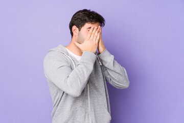 Young man isolated on purple background afraid covering eyes with hands.