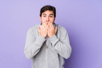 Young man isolated on purple background shocked, covering mouth with hands, anxious to discover something new.