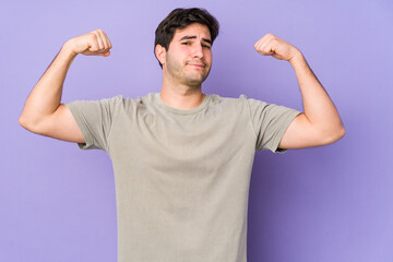 Young man isolated on purple background showing strength gesture with arms, symbol of feminine power