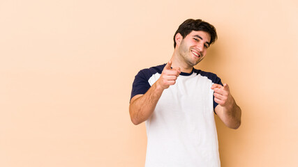 Young man isolated on beige background pointing to front with fingers.