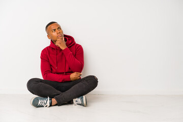 Young latin man sitting on the floor isolated looking sideways with doubtful and skeptical expression.