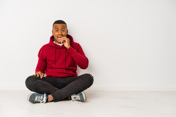 Young latin man sitting on the floor isolated biting fingernails, nervous and very anxious.