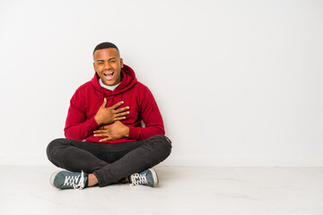 Young latin man sitting on the floor isolated laughs happily and has fun keeping hands on stomach.