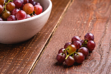 Fresh ripe grape berries in bowl on brown wooden background, angle view selective focus