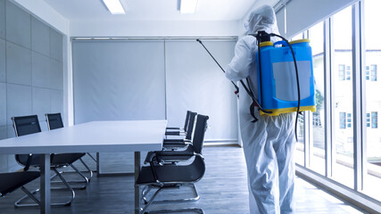 Worker in personal protective equipment (ppe) suit cleaning in building with spray disinfectant...