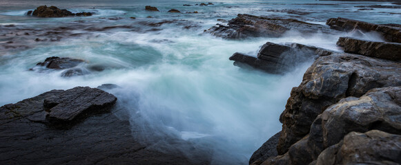 the power our oceans, closeup photography of the waves hitting into the rocks, and the water splashing up into the air during the sunset with beautiful cloudscape in the background 