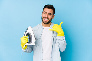 Portrait of young man ironing isolated showing a mobile phone call gesture with fingers.