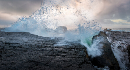the power our oceans, closeup photography of the waves hitting into the rocks, and the water splashing up into the air during the sunset with beautiful cloudscape in the background 