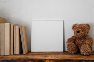 Mockup template with empty white frame, vintage books and teddy bear.