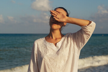 Young woman close her eyes with her hand the background of the sea. The girl is resting in a warm country.