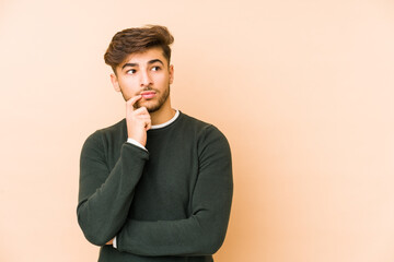 Young arabian man isolated on a beige background looking sideways with doubtful and skeptical expression.