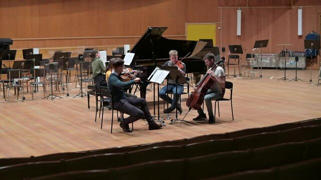 a string quartet with a grand piano rehearsing before the performance. Five musicians on stage in the orchestra hall