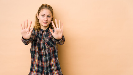 Young caucasian woman isolated on beige background showing number ten with hands.