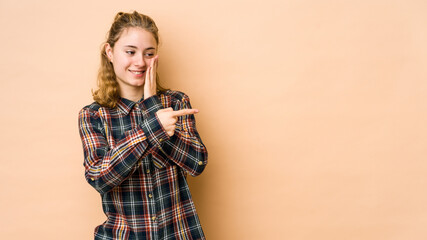 Young caucasian woman isolated on beige background saying a gossip, pointing to side reporting something.