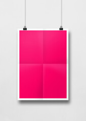 Pink folded poster hanging on a white wall with clips