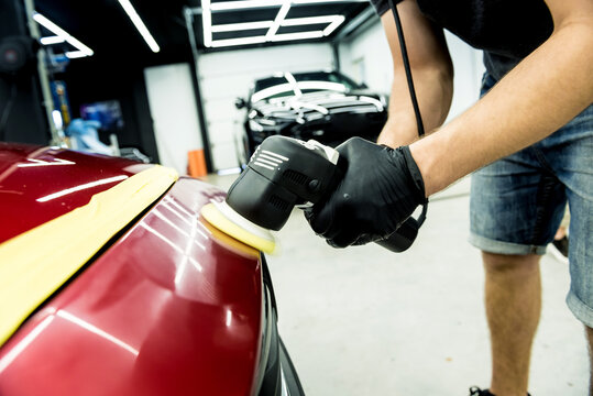 Car service worker polishes a car details with orbital polisher.