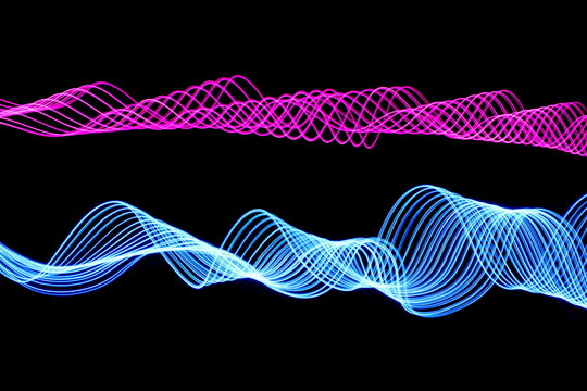 Long exposure photograph of neon pink and blue colour in an abstract swirl, parallel lines pattern against a black background. Light painting photography.