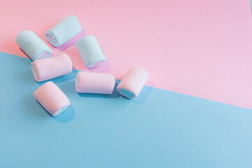 3pink and 3 blue marshmallows are scattered over a pink and blue background.Photo in pastel colors, close-up,soft focus.Idea-background,advertising space, text space,mockup,postcard,invitation,yummy.