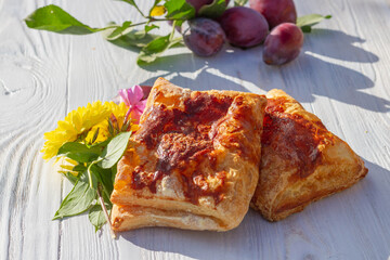 Delicious puffs, plum pies are on the table in autumn. Fragrant fresh pastries with fresh plum berries on a white Board.