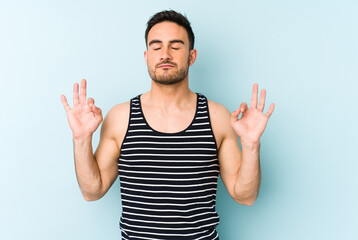 Fototapeta premium Young caucasian man isolated on blue background relaxes after hard working day, she is performing yoga.