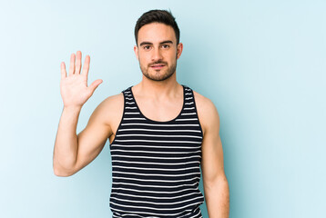 Young caucasian man isolated on blue background smiling cheerful showing number five with fingers.