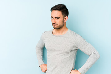 Young caucasian man isolated on blue background frowning face in displeasure, keeps arms folded.