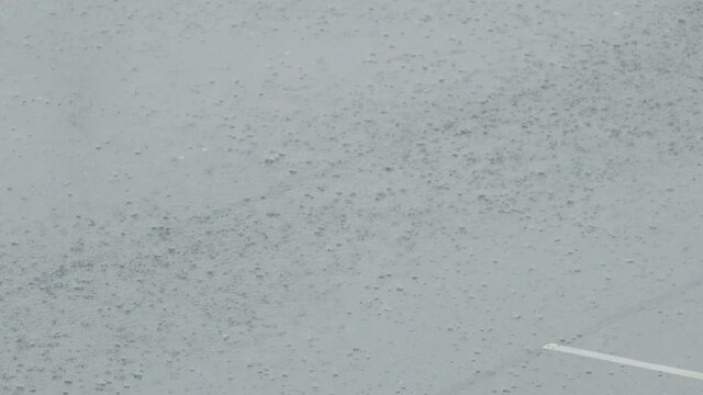 Slow motion pan of rain falling on wet asphalt paking