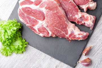 Several sliced steaks of pork neck on black stone board with ingredient on gray kitchen table. Close up view.