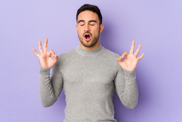 Naklejka premium Young caucasian man isolated on purple background relaxes after hard working day, she is performing yoga.
