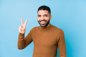 Fototapeta premium Young latin man against a blue background isolated showing victory sign and smiling broadly.