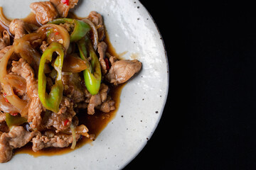 Stir-fried pork bell pepper in a white plate on a black background.