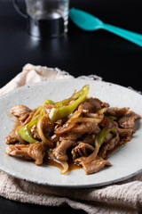 Stir-fried pork bell pepper in a white plate on a black background.