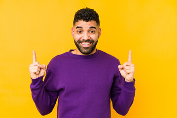 Young mixed race arabic man isolated indicates with both fore fingers up showing a blank space.