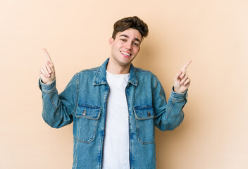 Young caucasian man isolated on beige background pointing to different copy spaces, choosing one of...