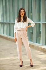 Obraz premium Young beautiful brunette woman in white blouse and pink pants in office