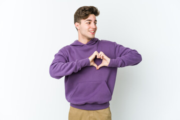 Young caucasian man isolated on white background smiling and showing a heart shape with hands.